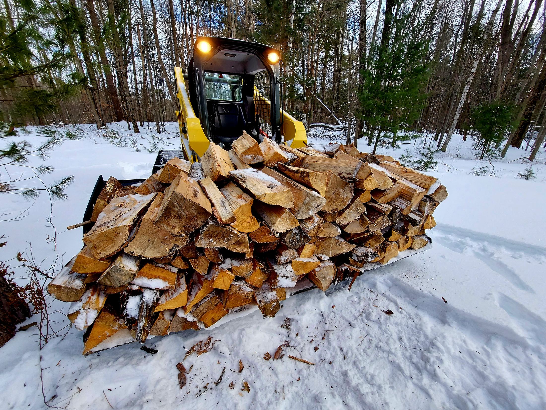 High Volume Material Bucket carrying a load of firewood through the snow