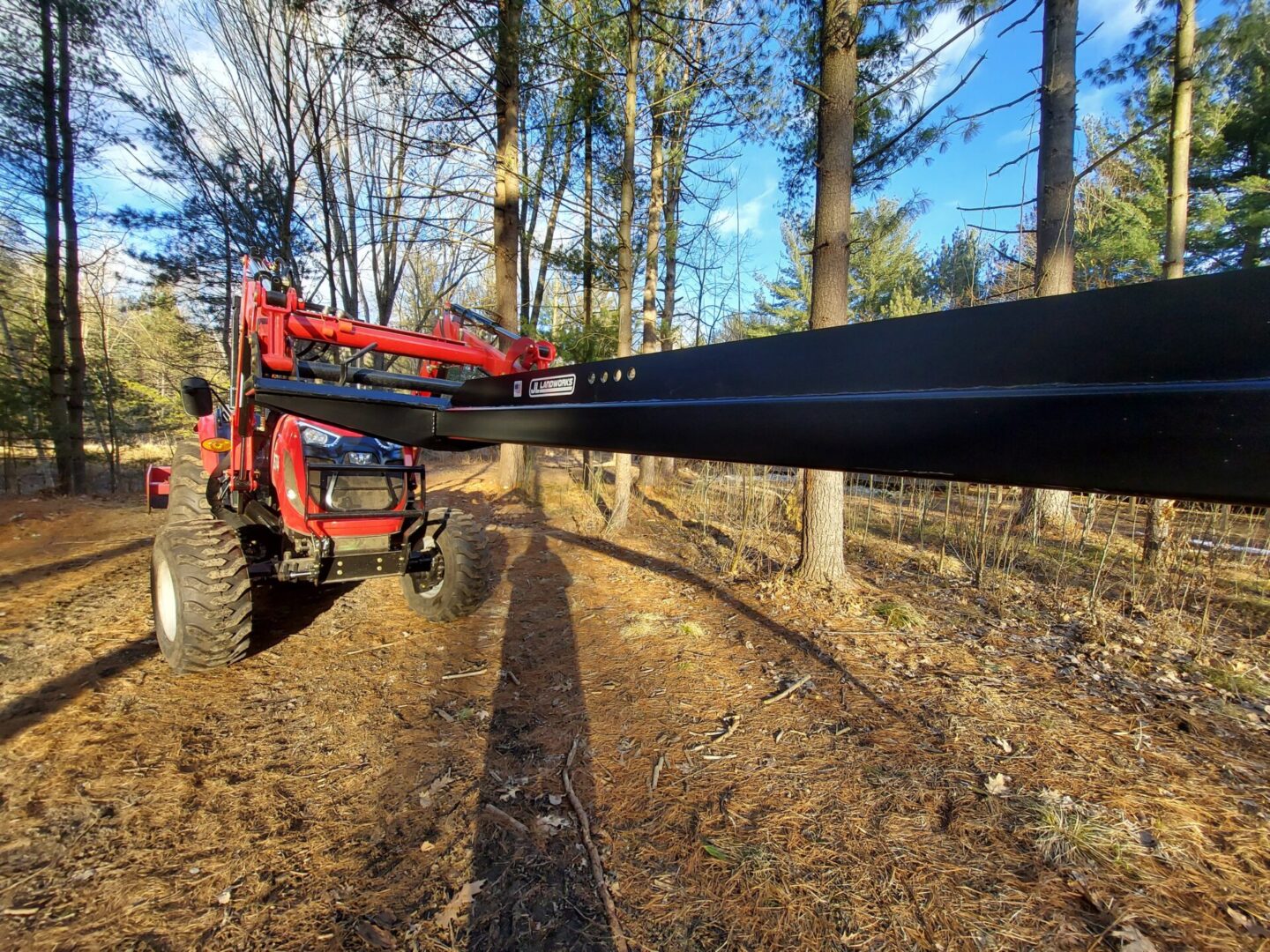 A tractor pulling a large pole in the middle of a forest.