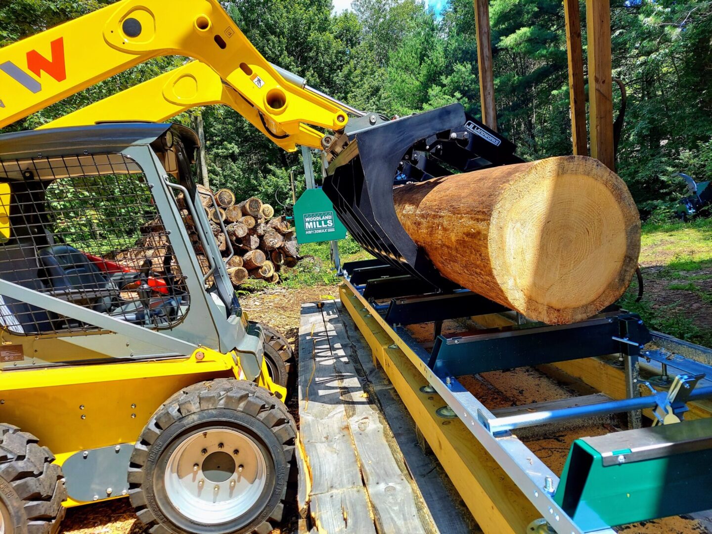 A yellow tractor is loading logs on to the trailer.