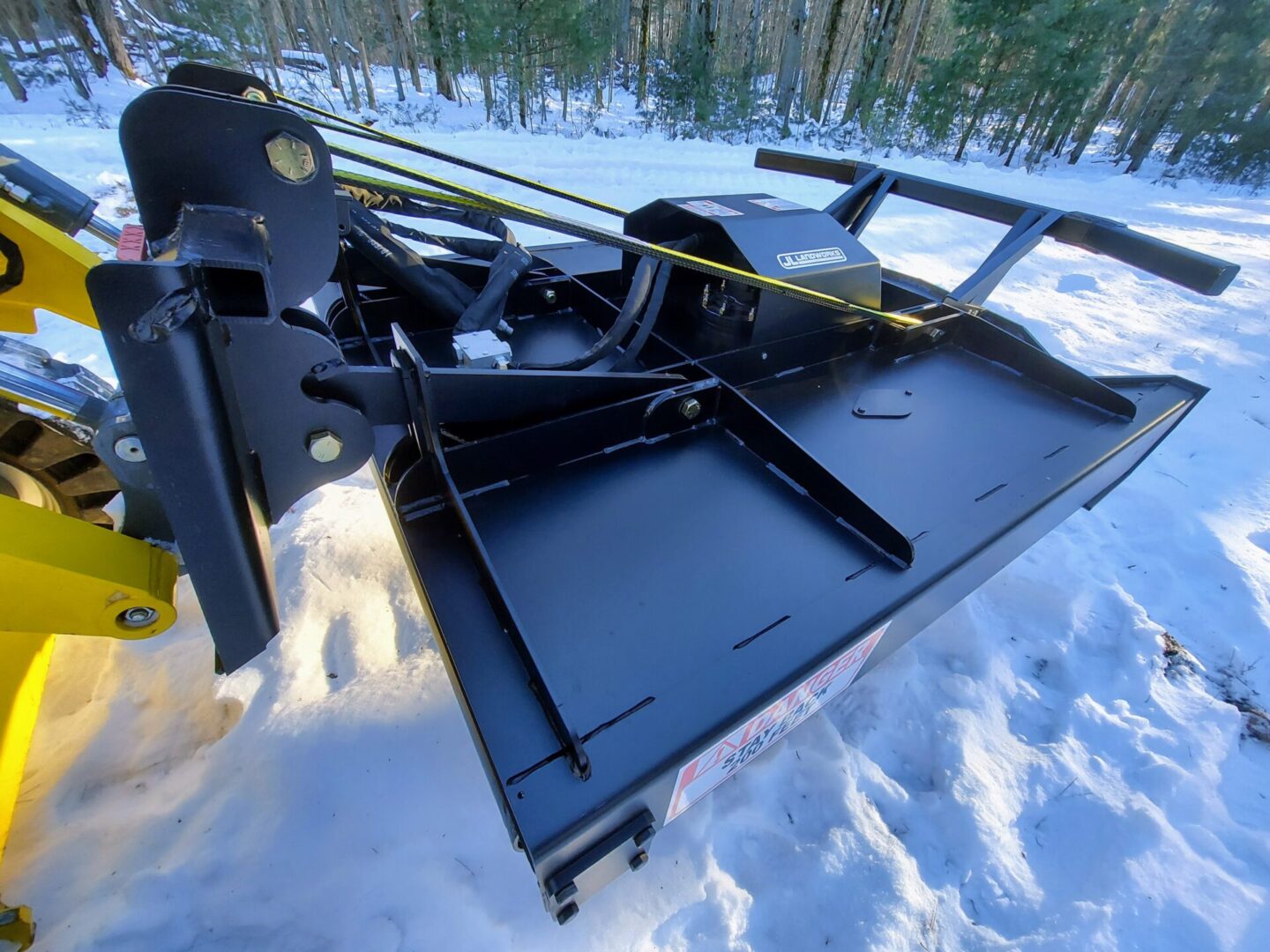 A black plow sitting in the snow next to trees.