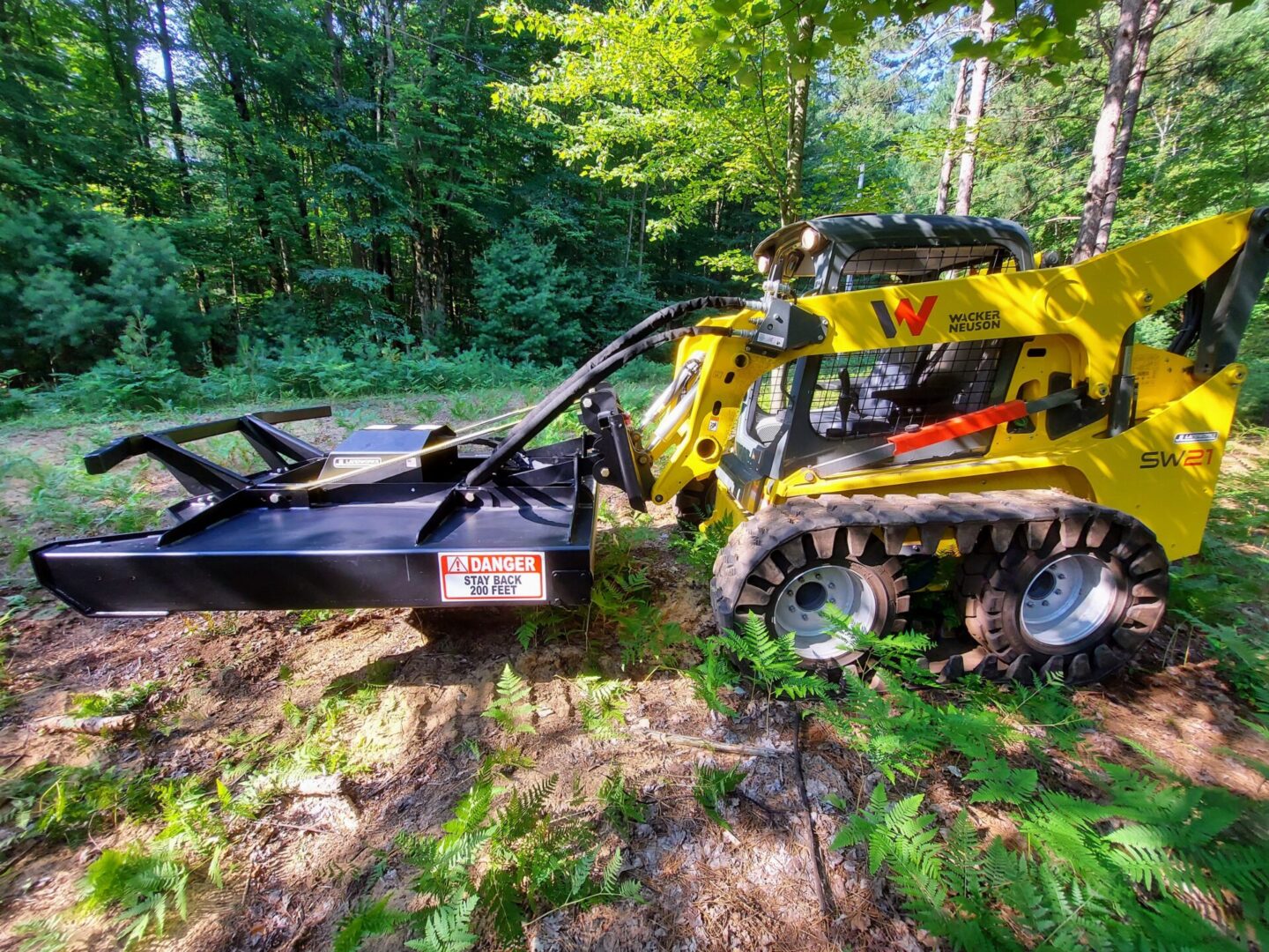 A yellow tractor with a plow in the middle of a forest.