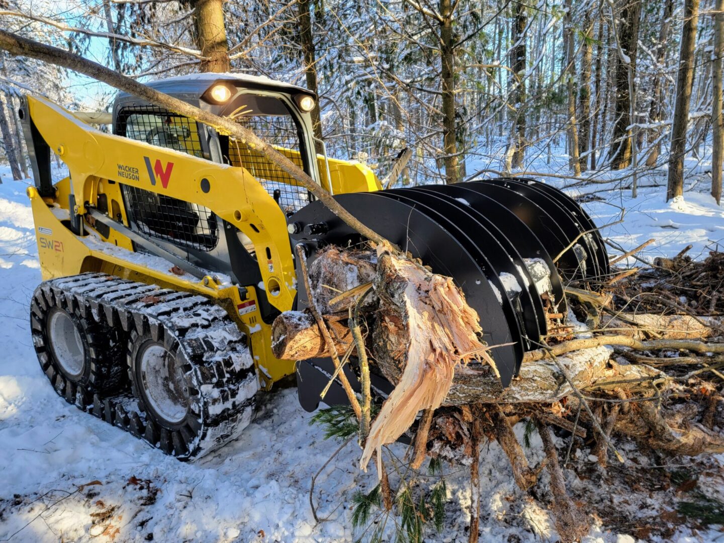 A yellow tractor is pulling logs in the snow.