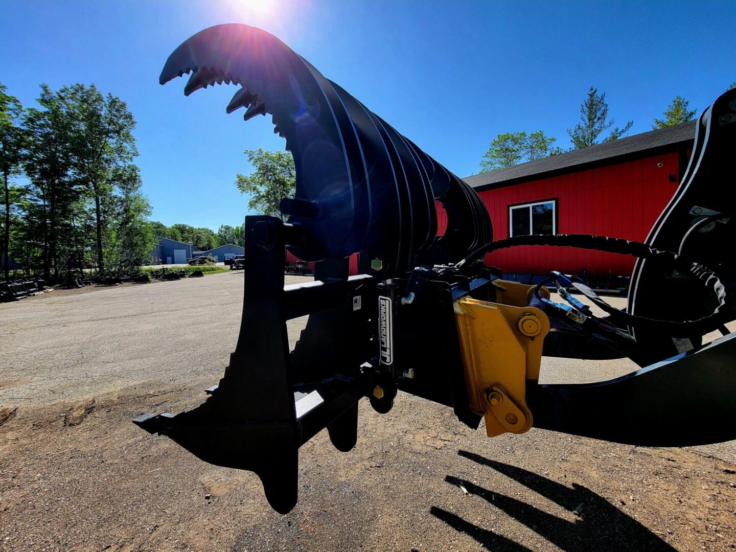 A black plow sitting in the dirt near a red building.