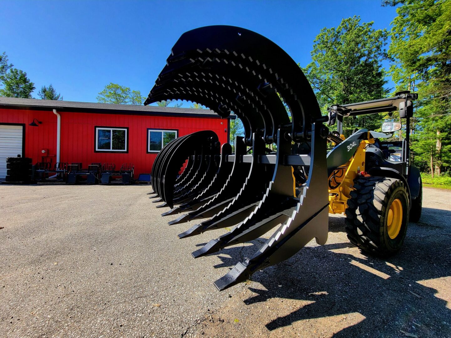 A tractor with many large metal blades in front of a red building.