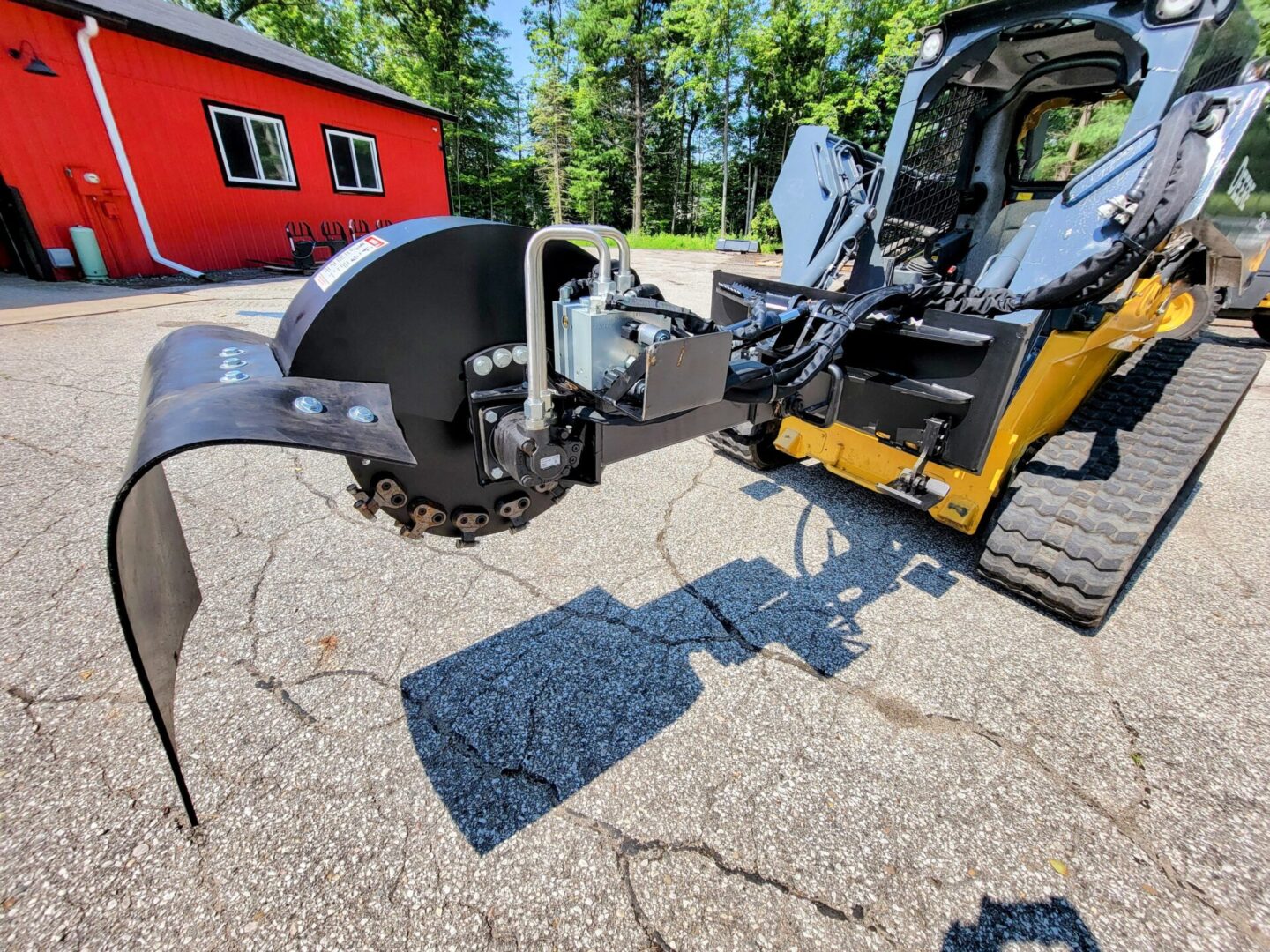 A yellow and black tractor with a red house in the background.