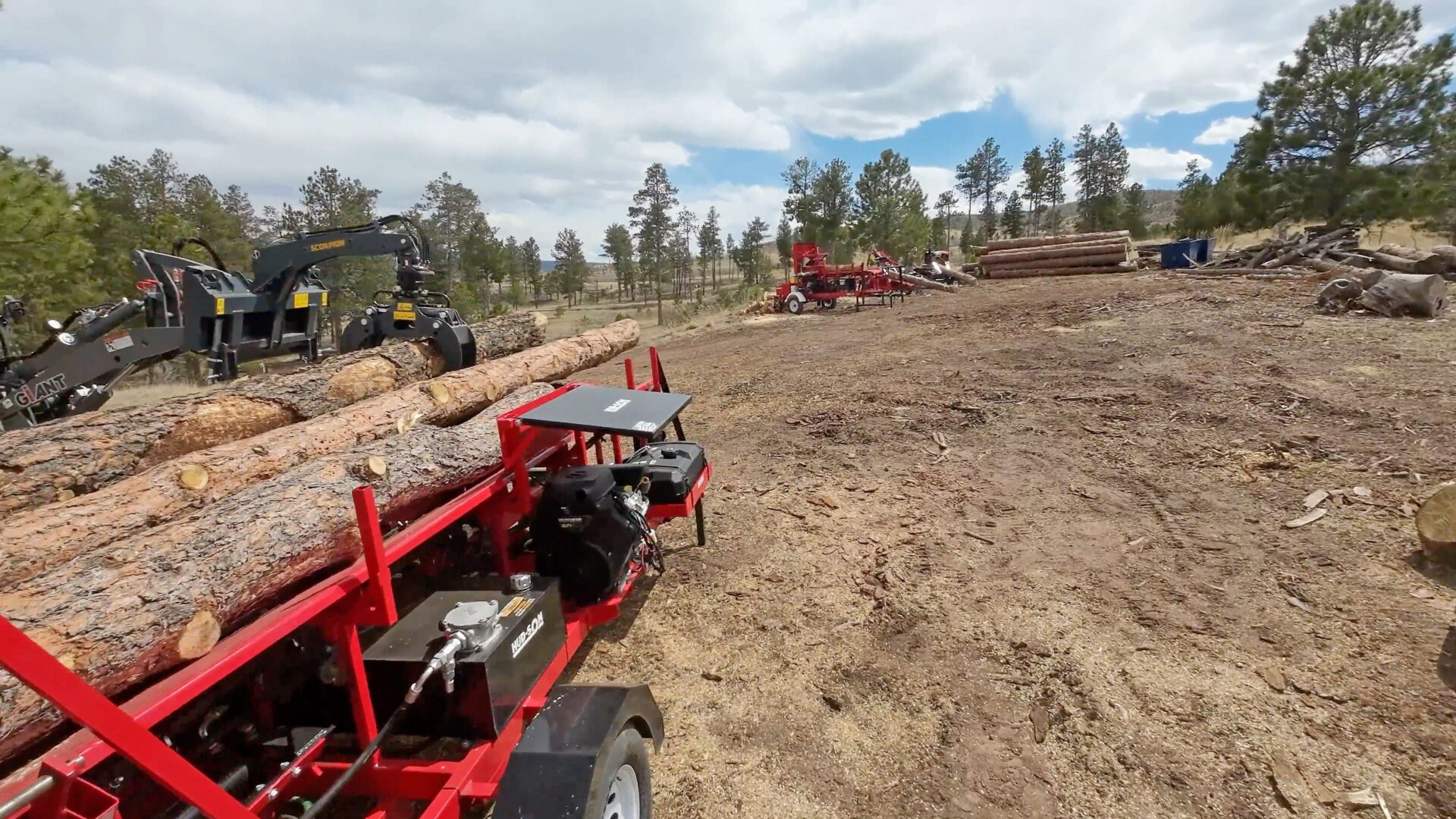 A red trailer with logs on it in the dirt.