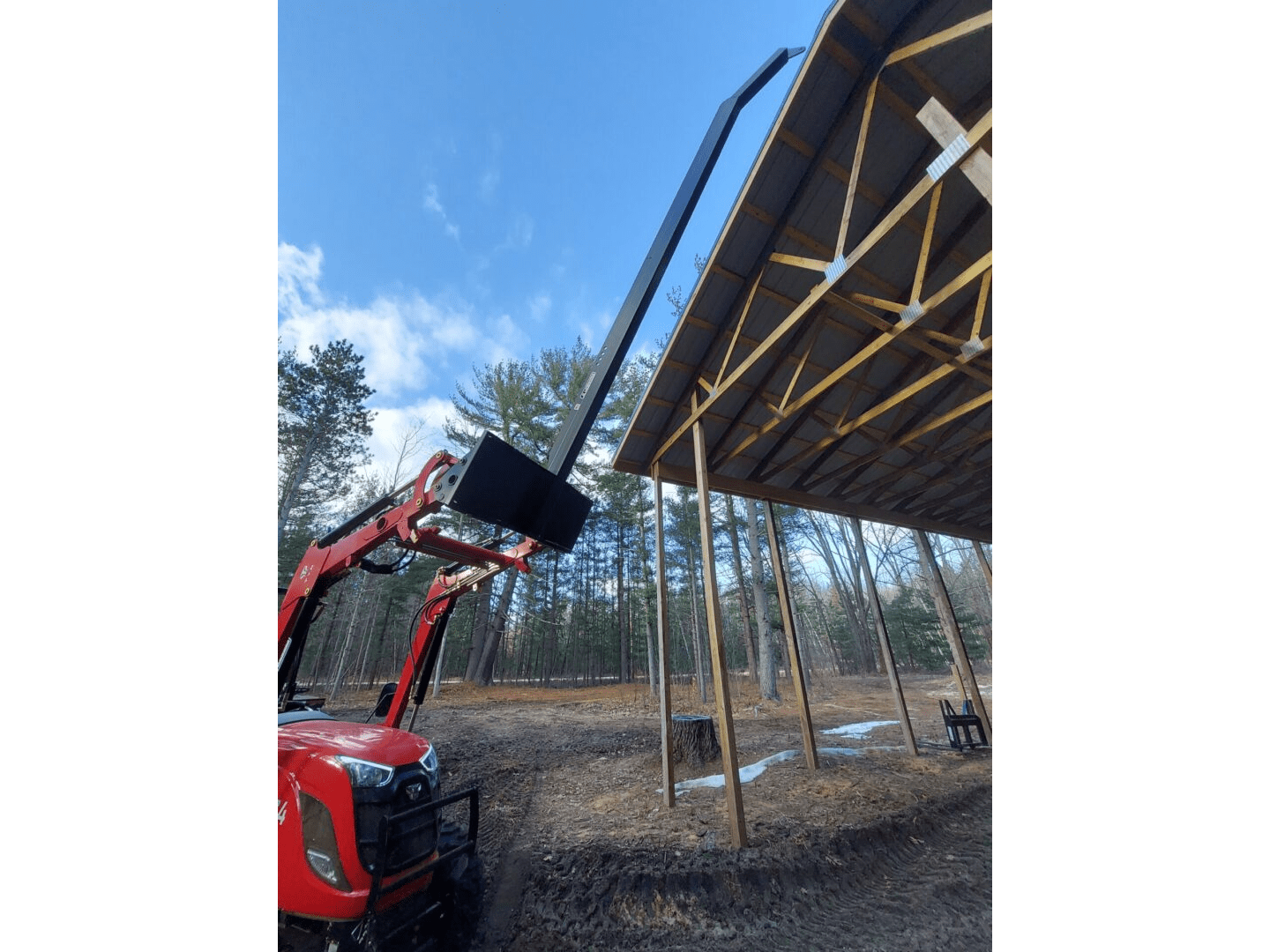 A red tractor is parked in front of a wooden structure.